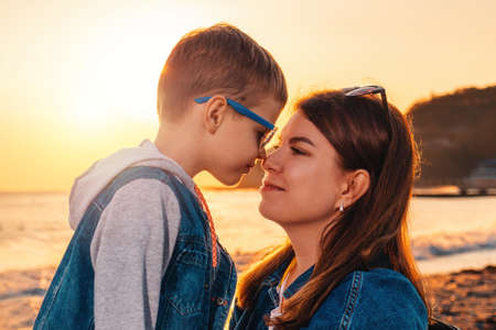 Portrait of young smiling mother and her son. In the background is the sea and sunset. The concept...