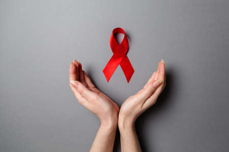 Female's hands frame a red ribbon, a symbol of the fight against AIDS. Gray background. Flat lay....