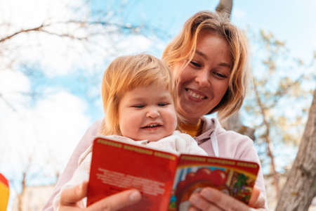 Happy young mother reads a book to her little daughter while relaxing in the park. Bottom view. The...