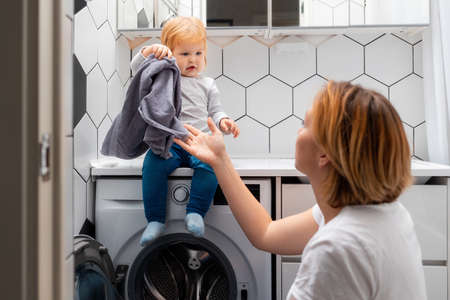 A mother and her little daughter loading laundry in the washing machine together.の写真素材