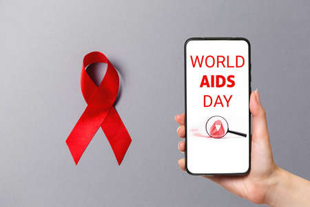 Know your status. A red ribbon on the gray background. Hand holding a smartphone. The concept of...