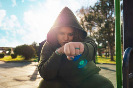 Portrait of overweight self-confident woman in a sportwear showes a fist sitting on exercise equipment. Concept of girl power.の写真素材