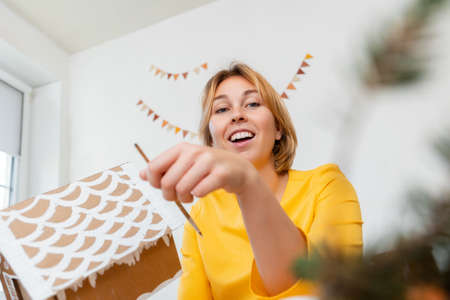 Portrait of smiling young woman is decorating a cardboard house. Handmade crafts for the Christmas holidays. Bottom view.の写真素材
