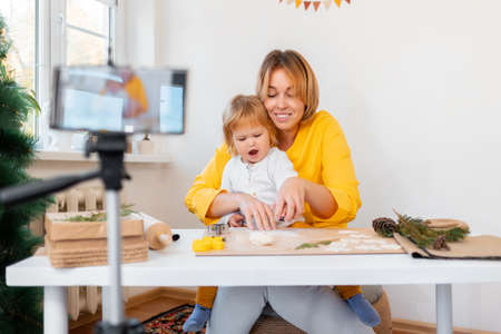 Portrait of young mother and her little daughter are making toys for the Christmas holidays. Defocused smartphone on the foreground. The concept of video streaming.の写真素材