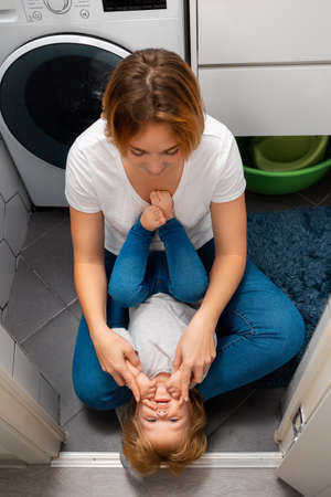 Happy mother and her little daughter play together in the bathroom, sitting on the floor. Happy childhood.の写真素材