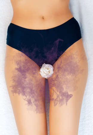 A woman in black panties with a white rose in the intimate area. A lilac cloud symbolizing an unpleasant smell. Close-up. Vertical. The concept of gynecology and female's diseases.の写真素材