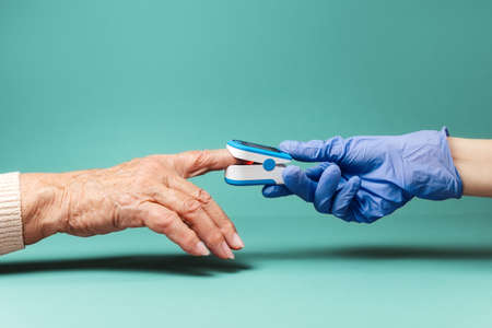 Doctor puts an oximeter on the index finger of an senior woman. Hands close-up. The concept of modern medical diagnostics.の写真素材