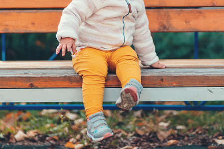 A small child is sitting alone on a bench, legs in close-up. The concept of lost children and an orphanage.の写真素材