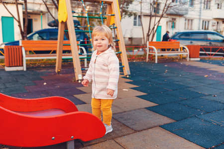 A little cute girl is standing near the children's slide on the playground. The concept of childhood and autism.の写真素材