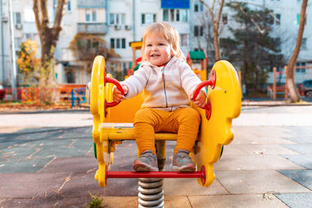 Portrait of a little happy girl rolling on a swing, on a playground. The concept of a happy childhood and children's Day.の写真素材