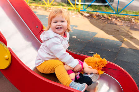 A happy little girl is sitting on a children's slide with her toy. The concept of Children's Day and happy childhood.の写真素材