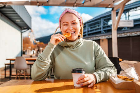 Portrait of a young smiling woman with dreadlocks eating dried orange a and drink coffee in cafe. Concept of natural sugar free sweets.の写真素材