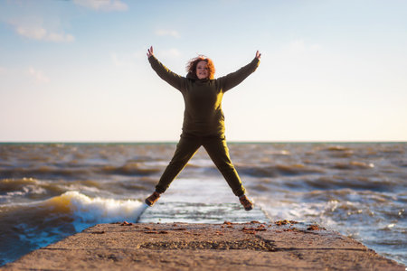 A full happy woman jumps on the pier and by the sea. Sky and ocean in the background. The concept of psychology and success.の写真素材