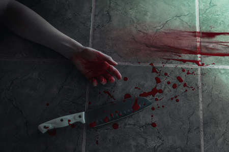 Big sharp kitchen knife with blood, female hand of victim and bloody traces. Weapon and person lies...
