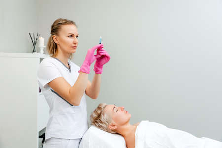 A woman is receiving a procedure from a cosmetologist. A specialist prepares a syringe with an injection for the client. Rejuvenation procedure in salon.の写真素材
