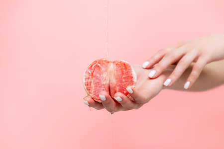 Woman's elegant hands hold half a grapefruit. Oil is poured on top of the fruit. Copy space. The concept of sexuality.の写真素材