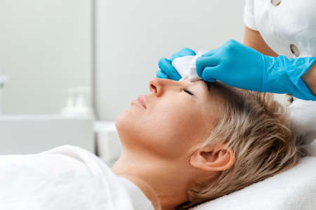 Professional care in beauty salon. Cosmetologist does a deep mechanical cleaning of the client's face. Side view. Acne concept.の写真素材