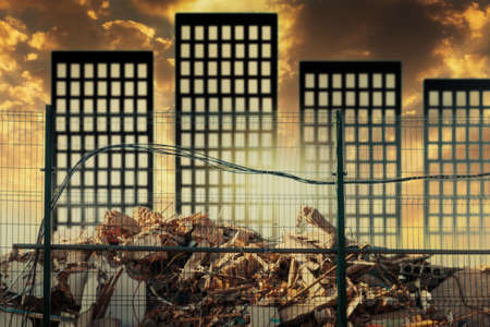 The ruins of a destroyed buildings behind the fence. Against the background of the sunset sky and silhouettes of high-rise buildings. Bottom view. Slum demolition conceptの写真素材