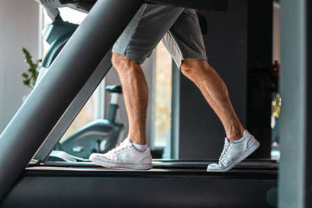 International Day of Sport. Close up of feet of sporty man training on a treadmill. Side view.
