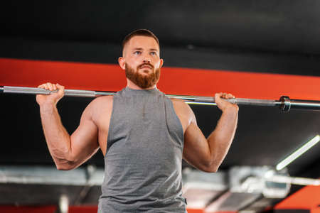 A young bearded athletic man trains in the gym, lifting a barbell. Bottom view. The concept of...