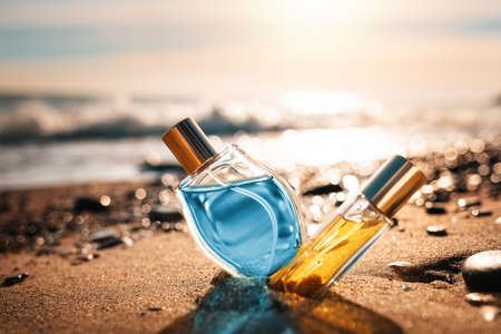 Two glass bottles of golden and blue perfumes on the sandy seashore. Narrow and rounded vials.の写真素材
