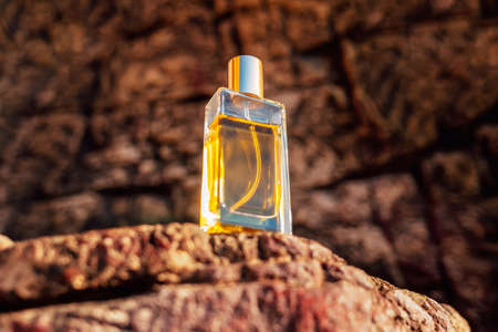 Perfumery. A glass transparent bottle of golden perfume standing on a brown stone. Bottom view. Copy spaceの写真素材