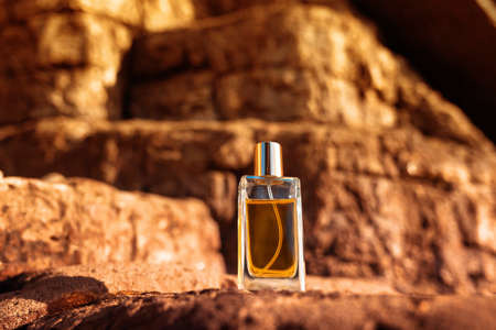 Perfumery. A glass transparent bottle of golden perfume standing on a brown desert stone. Sunset lighting. Bottom viewの写真素材
