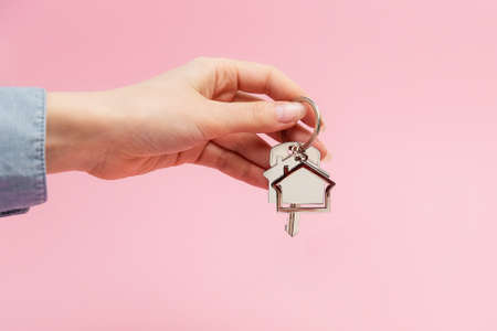 Female hand holding key and house keychain. Pink background with copy space. Concept of mortgage and...