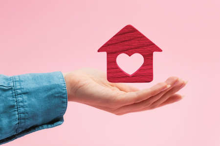 Mortgage. A red wooden house with a heart hovers over a woman's palm. pink background. The concept of leasing, insurance and home purchase.の写真素材