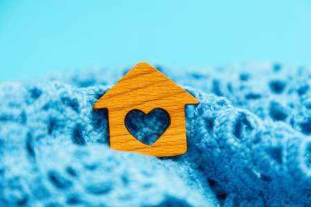 Close-up of a little wooden house with a heart lying in a knitted scarf. blue background. The concept of leasing, home purchase and mortgage.の写真素材