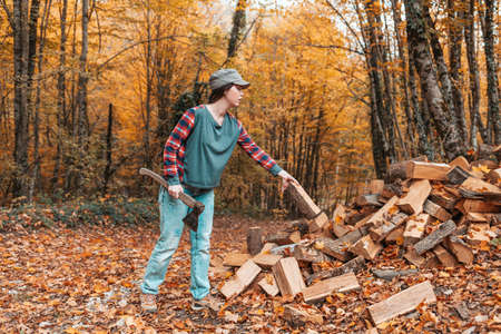 Preparation for the heating season. A young woman with an ax in her hands throws a log into a pile of logs. In the background autumn forest.の写真素材