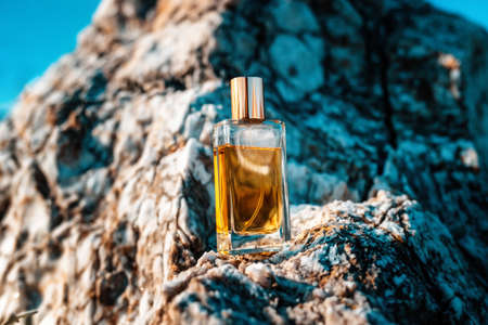 A glass transparent rectangular bottle of golden perfume standing on a gray marble stone. perfumery...