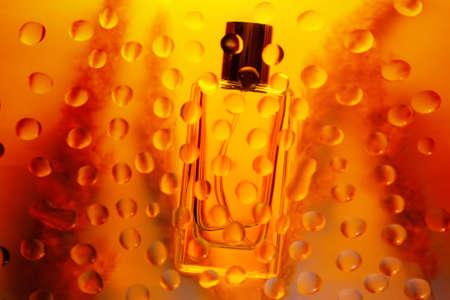 Glass transparent rectangular perfume bottle on a golden background with a silhouette of stalks. A...