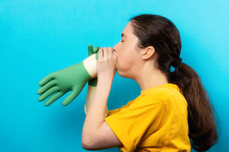 Portrait of a Caucasian woman in profile, inflating a rubber glove. blue background. Cleaning...