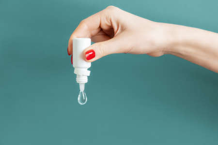 A beautiful female hand with a red manicure holds the medicine, squeezing a large drop down. Green...