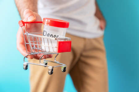 A man is holding a small cart with a jar of sperm in his hand for analysis. close-up. The concept of sperm donation and artificial insemination.の写真素材