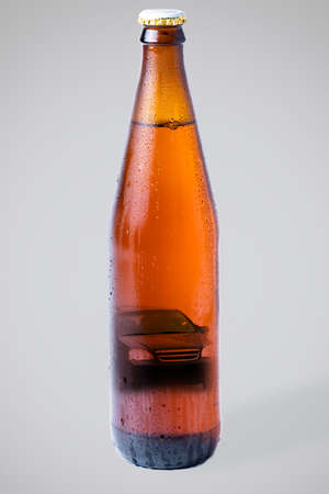 Wet bottle of dark beer with a picture of a car inside. Gray background, vertical orientation. The concept of drunk driving and alcoholism.の写真素材