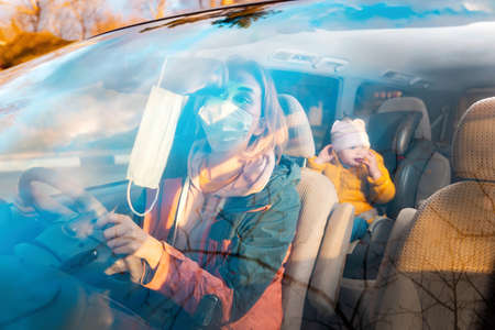 Portrait of a woman in a protective mask, sitting at the wheel of a right-hand car and looking...