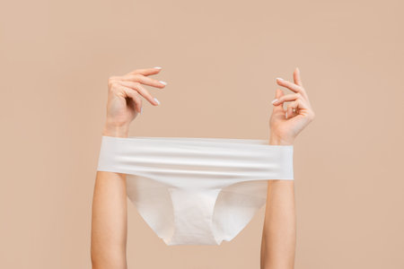 Elegant female hands with panties stretched over them. Beige background. copyspace. The concept of...
