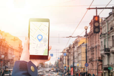 A woman's hand in a jacket holds a smartphone with an online map app. In the background is a city...