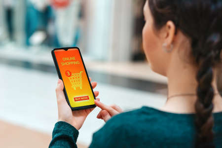 A woman holds a smartphone with an open page in an online store. Close-up view from over the...