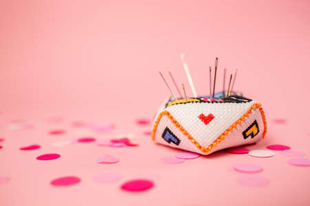 Clsoe up of pincushion with hearts on a pink background with confetti. copyspace. Handmade gifts for Valentine's Day.の写真素材