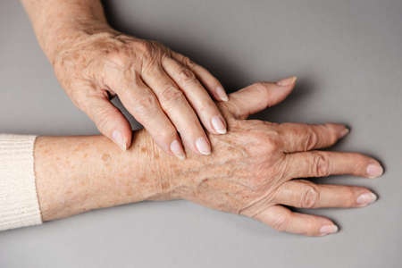 Close up of elderly woman massages her hands, experiencing pain. gray background. flat lay. The concept of rheumatism and arthritis.の写真素材