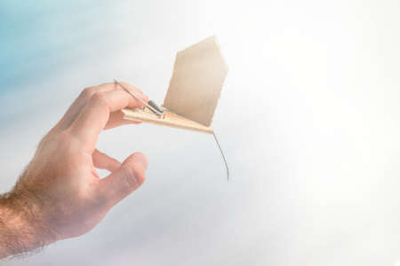 Bank investments and risks. A man's hand was caught in a mousetrap with a schematic cardboard house. In the background, heaven and light. copyspace.の写真素材
