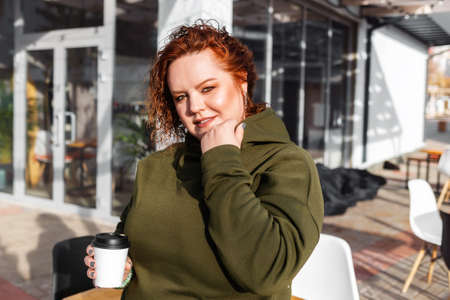 Portrait of a overweight smiling woman posing with a cup of coffee in her hand. Cafe at the background. Concept of psychology.の写真素材