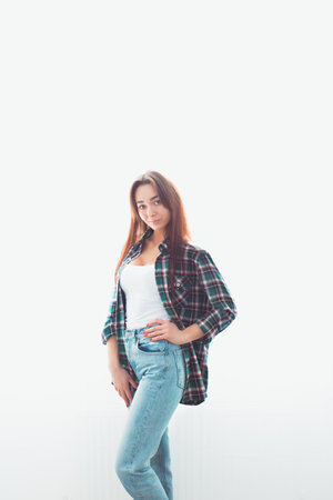 Portrait of a young slender brunette woman in casual clothes posing on a white background. Behind...