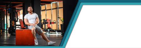 Banner of fitness with mock up. Handsome athletic bearded man poses sitting on a cube in modern gym....
