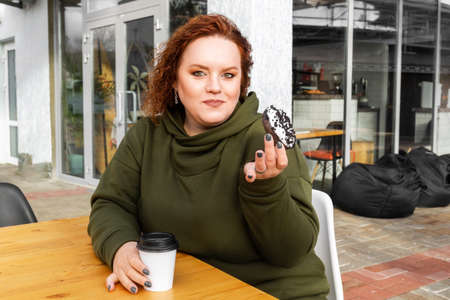 Portrait of overweight beautiful woman eating a chocolate donut at cafe. The concept of diet and...