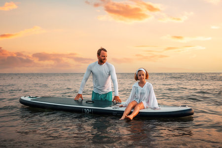 Father and daughter surfing on a sup board. Sea and sunset sky at the background. summer holidays....
