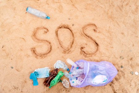 Trash bag with plastic bottles on a sandy beach. Text SOS on a sand. top view. The concept of environmental protection and conservation.の写真素材
